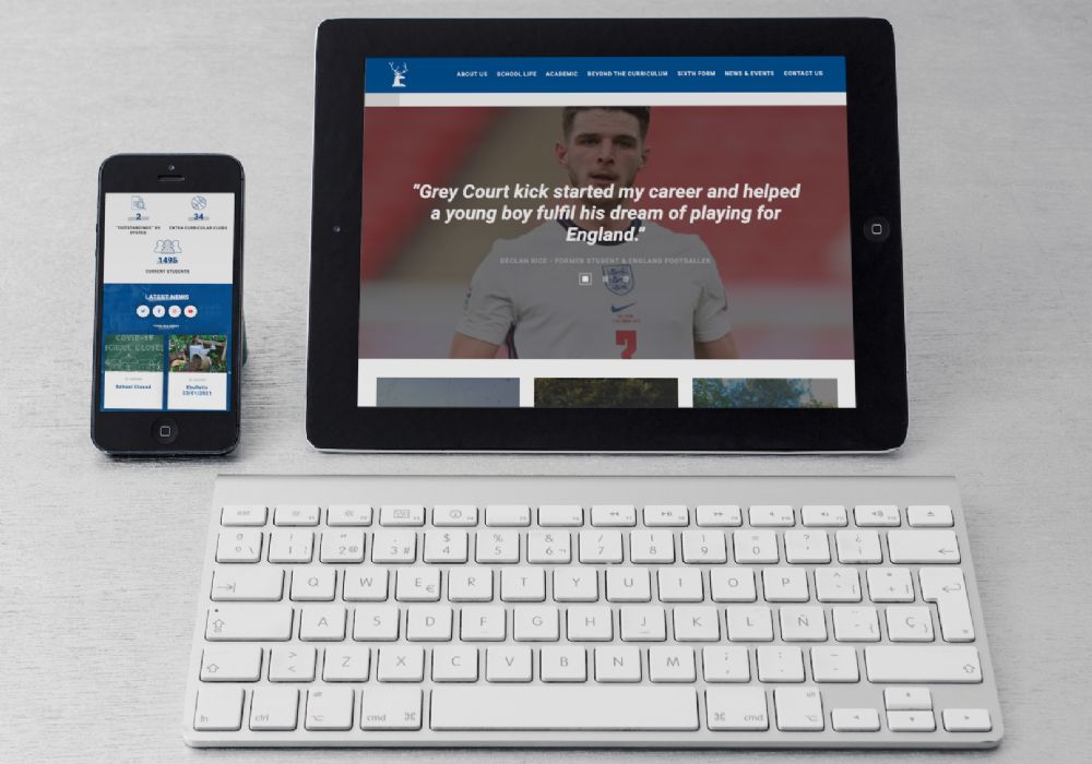 A tablet and phone showing Grey Court school's homepage and a keyboard on a white desk. 