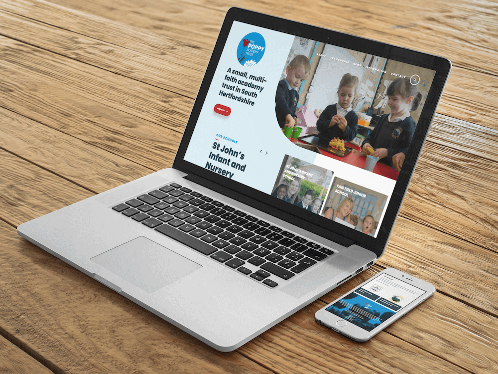 Poppy Academy Trust homepage on Macbook and phone laid on wooden bench